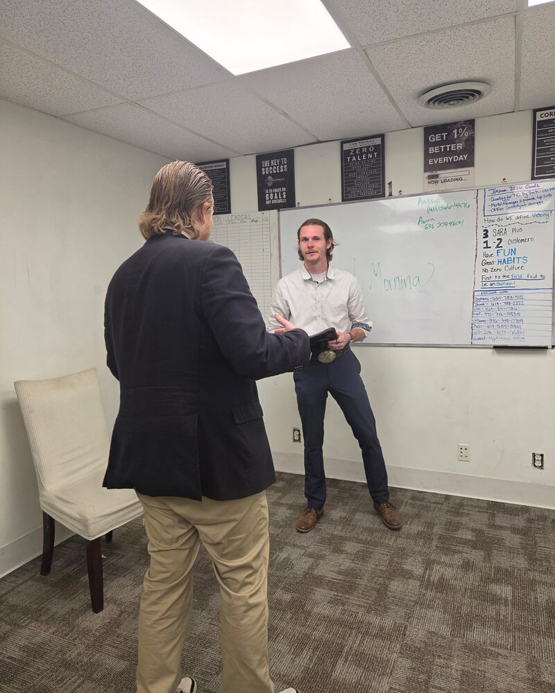 A sales coaching session in progress in front of the Atlas Marketing whiteboard